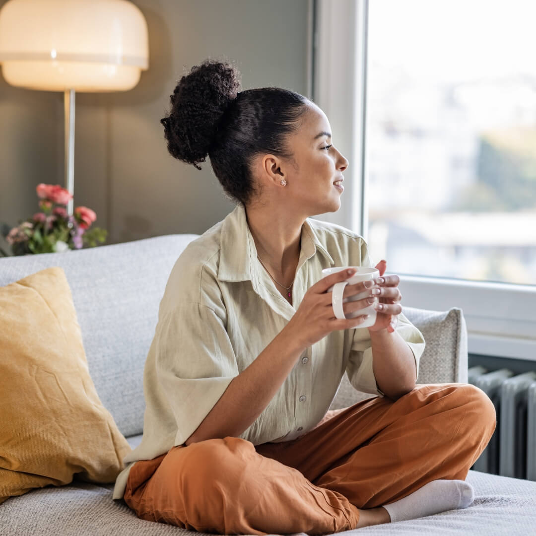  Relaxed woman sitting on a sofa with a cup of tea, symbolising calm, balance, and energy restoration through hypnotherapy and menopause coaching in Brisbane.