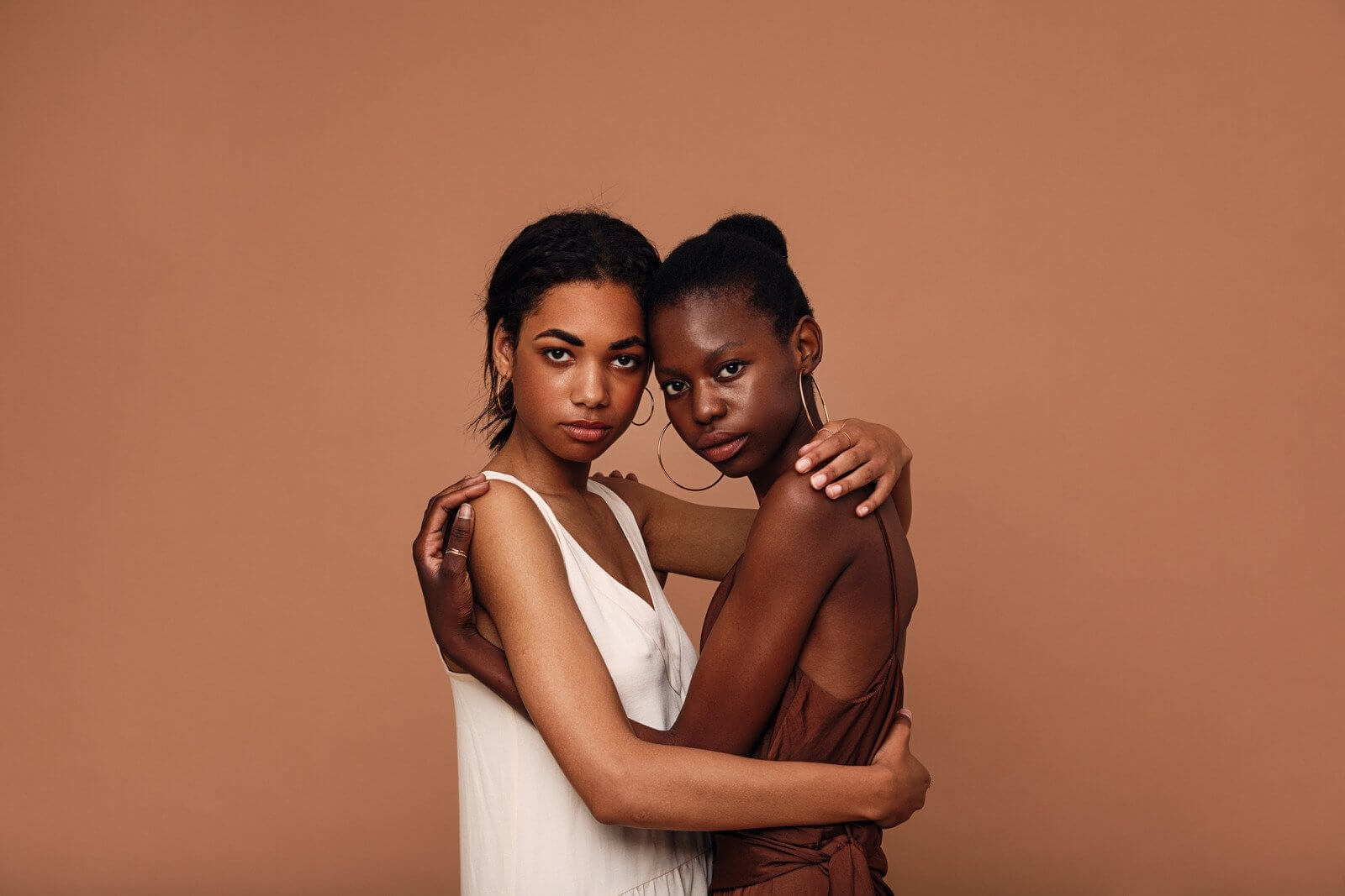 two individuals are hugging in front of a brown background